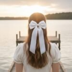 Stylish white bow headband worn in a half-up hairstyle by a woman at sunset.